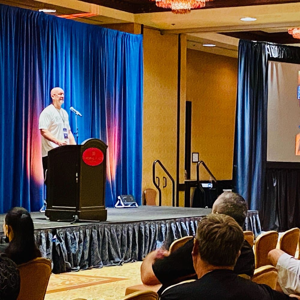 Coach Martens speaking from a podium to a room of coaches at a state coaching association conference
